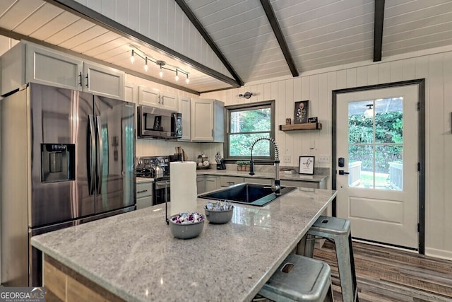 kitchen with light stone counters, sink, lofted ceiling, appliances with stainless steel finishes, and a kitchen bar