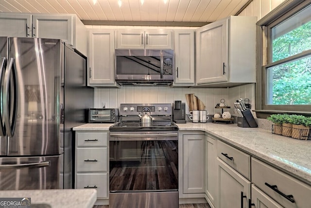 kitchen with light stone counters, hardwood / wood-style floors, wood ceiling, appliances with stainless steel finishes, and gray cabinets