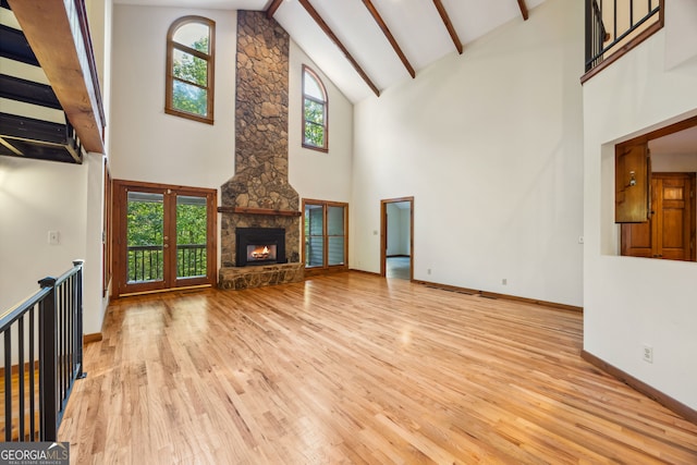 unfurnished living room with beam ceiling, high vaulted ceiling, light hardwood / wood-style flooring, and a fireplace