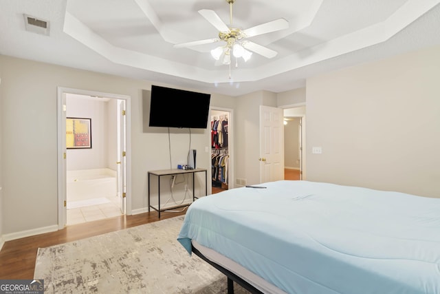 bedroom with a raised ceiling, ensuite bathroom, wood-type flooring, and a spacious closet