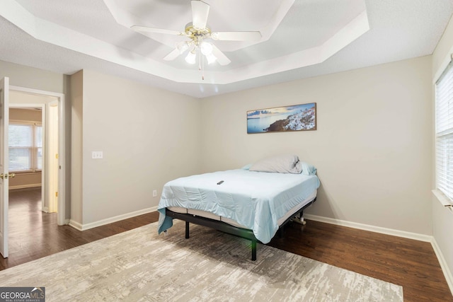 bedroom featuring dark hardwood / wood-style flooring, a tray ceiling, and ceiling fan