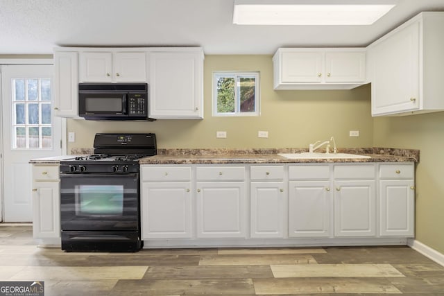 kitchen with black appliances, sink, dark stone countertops, light wood-type flooring, and white cabinetry