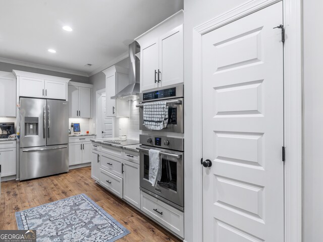 kitchen with wall chimney exhaust hood, stainless steel appliances, white cabinetry, and light hardwood / wood-style floors