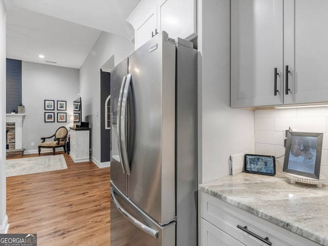 kitchen with light wood-type flooring, white cabinets, a fireplace, light stone countertops, and stainless steel fridge