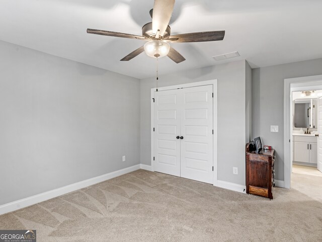 unfurnished bedroom with light carpet, ceiling fan, ensuite bathroom, and a closet