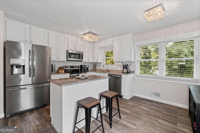 kitchen featuring appliances with stainless steel finishes, dark hardwood / wood-style floors, white cabinets, a breakfast bar area, and a center island