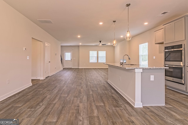 kitchen featuring a center island with sink, light stone countertops, dark hardwood / wood-style floors, gray cabinets, and stainless steel double oven