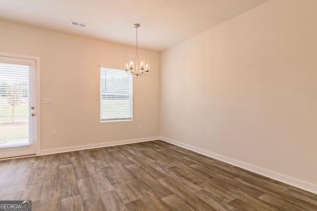 empty room with a wealth of natural light, a chandelier, and dark hardwood / wood-style floors