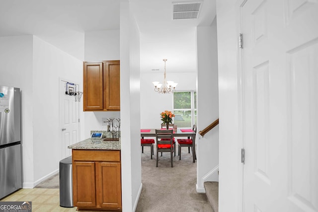 kitchen featuring stainless steel fridge, light stone countertops, pendant lighting, a chandelier, and light colored carpet