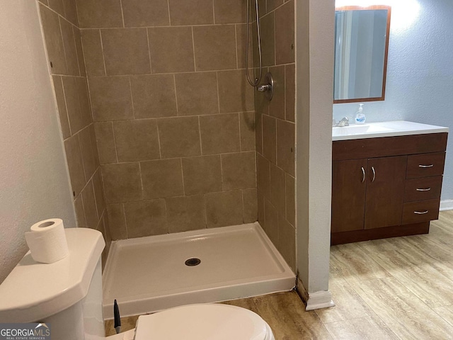 bathroom featuring vanity, tiled shower, hardwood / wood-style floors, and toilet