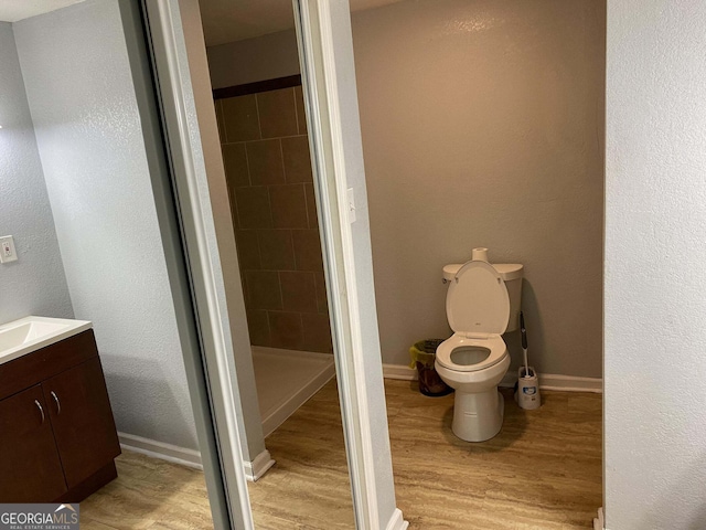 bathroom with a tile shower, vanity, toilet, and wood-type flooring