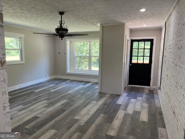 unfurnished living room featuring a wealth of natural light, dark hardwood / wood-style flooring, ceiling fan, and brick wall