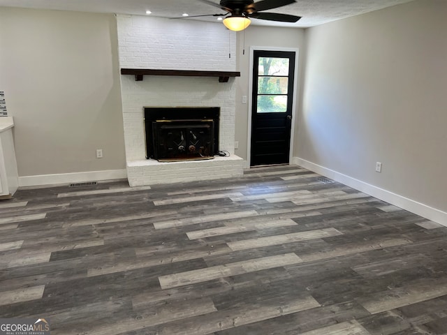 unfurnished living room featuring ceiling fan, a brick fireplace, and dark hardwood / wood-style flooring