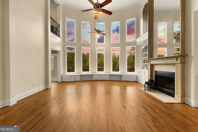 unfurnished living room with ceiling fan, radiator heating unit, a tile fireplace, light wood-type flooring, and crown molding