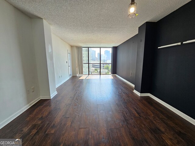 empty room with a textured ceiling, a wall of windows, and dark wood-type flooring