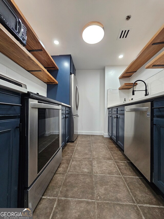 kitchen featuring sink, dark tile patterned floors, tasteful backsplash, blue cabinetry, and appliances with stainless steel finishes