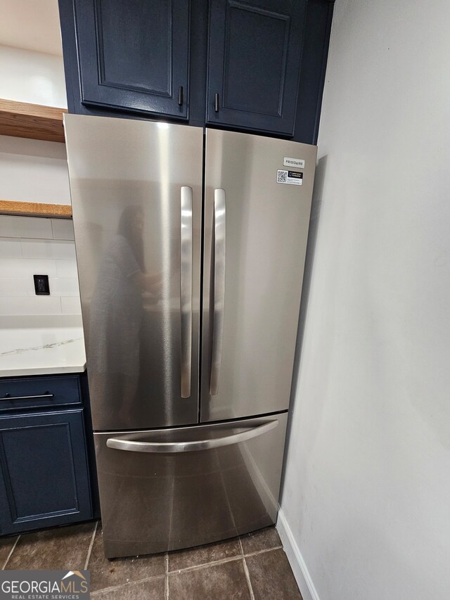 details with decorative backsplash, light stone counters, stainless steel refrigerator, blue cabinetry, and dark tile patterned floors