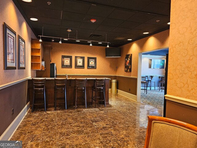 bar featuring rail lighting, stainless steel refrigerator, and a drop ceiling