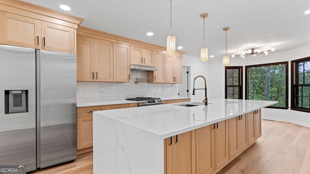 kitchen featuring light stone counters, hanging light fixtures, a center island with sink, appliances with stainless steel finishes, and light hardwood / wood-style floors