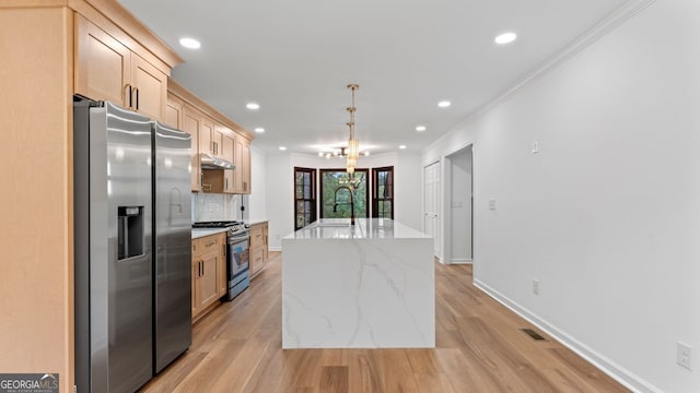 kitchen featuring light wood-type flooring, stainless steel appliances, a center island with sink, light brown cabinets, and crown molding