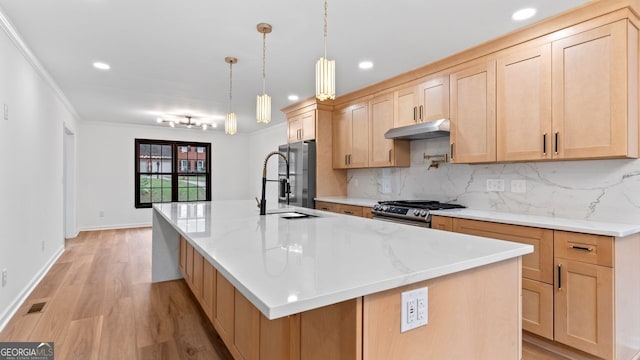 kitchen featuring pendant lighting, sink, a center island with sink, appliances with stainless steel finishes, and ornamental molding