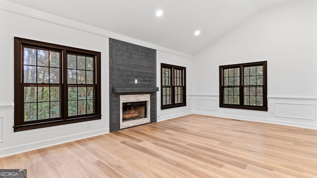 unfurnished living room with ornamental molding, light wood-type flooring, vaulted ceiling, and a fireplace