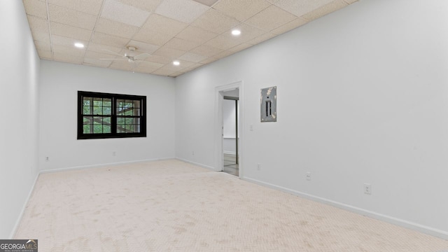 empty room featuring a paneled ceiling, electric panel, and light colored carpet