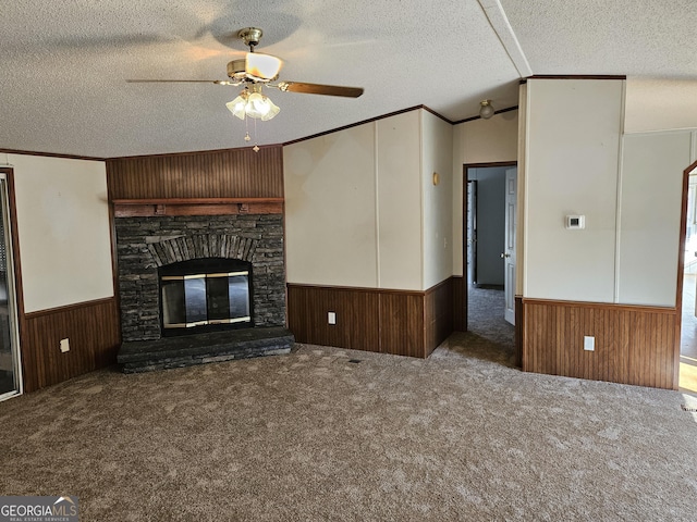 unfurnished living room featuring carpet, ceiling fan, a stone fireplace, and crown molding