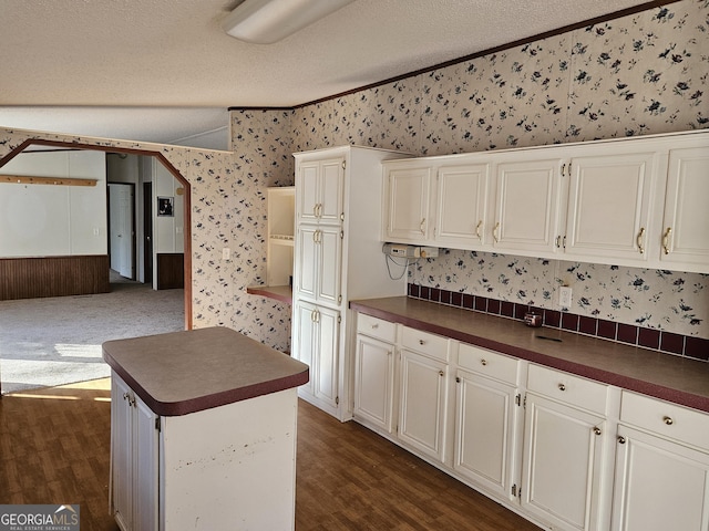 kitchen with ornamental molding, a textured ceiling, a center island, dark hardwood / wood-style floors, and white cabinetry