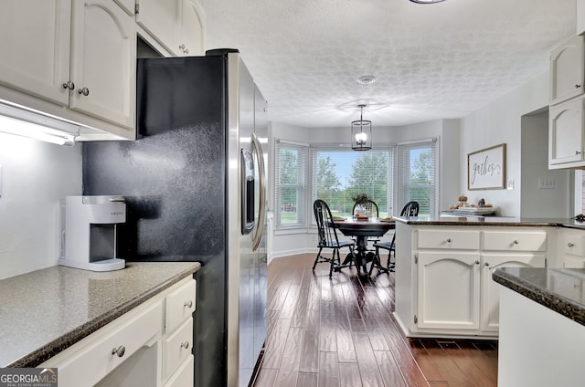 kitchen with hanging light fixtures, stainless steel fridge, a textured ceiling, white cabinetry, and dark hardwood / wood-style floors