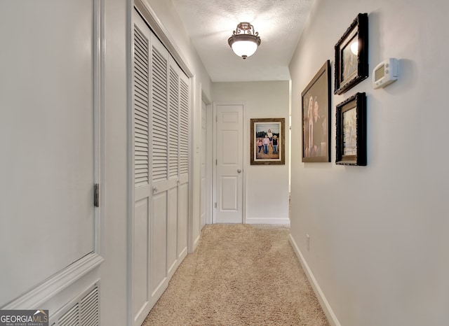 corridor with light colored carpet and a textured ceiling