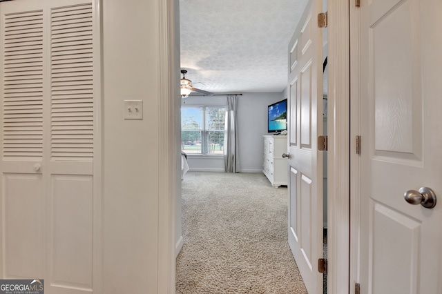 hallway with light colored carpet and a textured ceiling