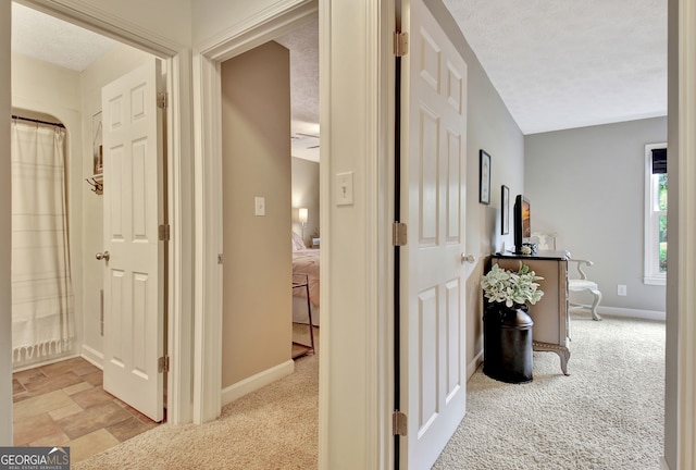 hall featuring light carpet and a textured ceiling