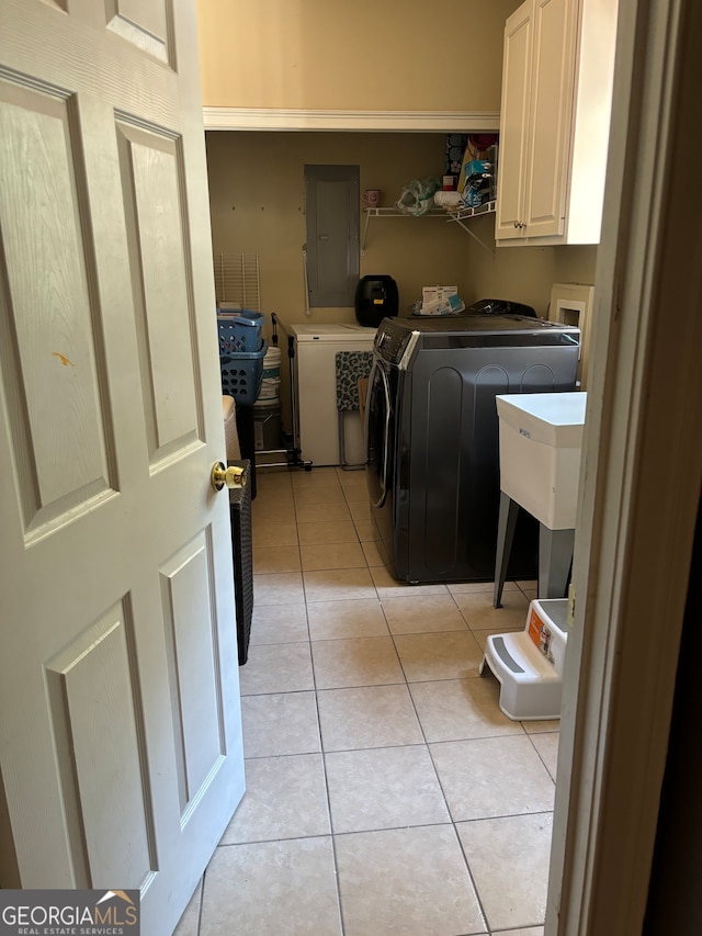 clothes washing area with washer and dryer, electric panel, light tile patterned floors, and cabinets