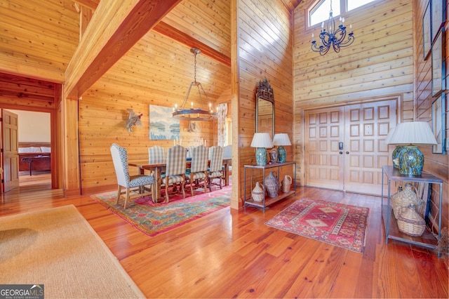 interior space featuring high vaulted ceiling, beamed ceiling, wood-type flooring, an inviting chandelier, and wooden walls