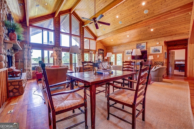 dining space featuring light wood-type flooring, a stone fireplace, ceiling fan, and high vaulted ceiling