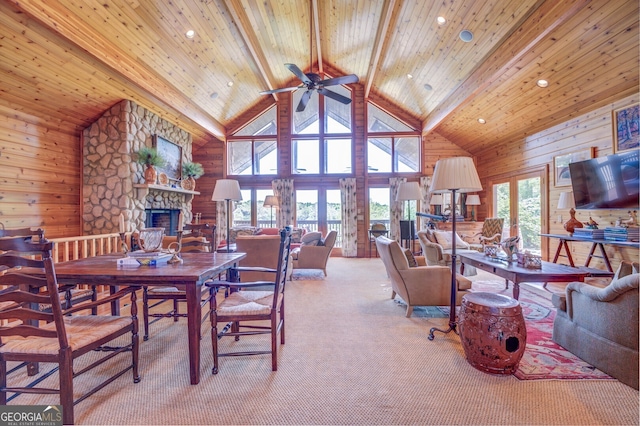 dining room with ceiling fan, beamed ceiling, wood walls, a stone fireplace, and high vaulted ceiling