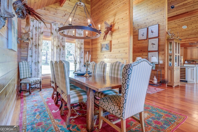 dining space featuring wooden walls, a chandelier, light hardwood / wood-style floors, and high vaulted ceiling