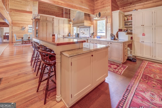 kitchen featuring a breakfast bar area, wooden walls, custom range hood, and a center island