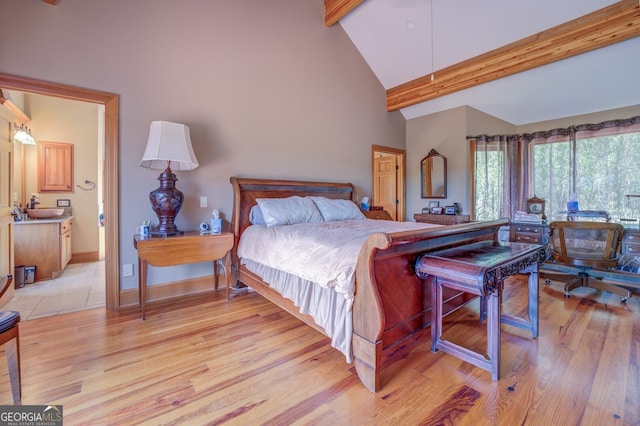 bedroom featuring high vaulted ceiling, beam ceiling, light hardwood / wood-style flooring, ensuite bath, and sink