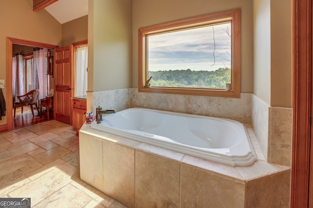 bathroom with lofted ceiling with beams and tiled tub