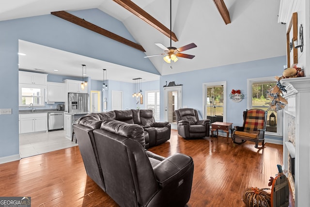 living room with beamed ceiling, ceiling fan with notable chandelier, light hardwood / wood-style flooring, sink, and high vaulted ceiling