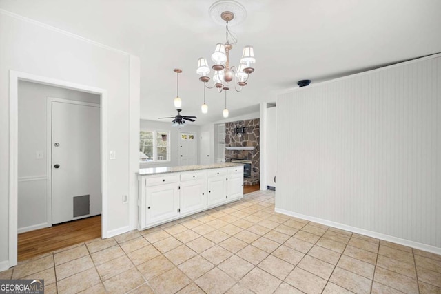 interior space featuring white cabinets, light tile patterned flooring, hanging light fixtures, a stone fireplace, and ceiling fan with notable chandelier