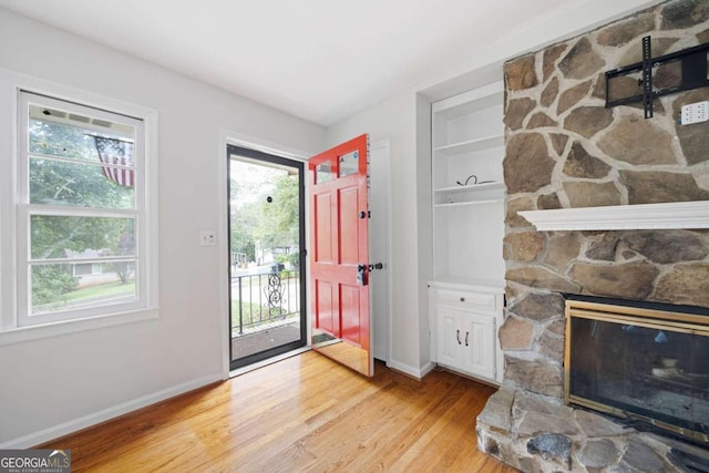 foyer entrance with light hardwood / wood-style floors and a stone fireplace