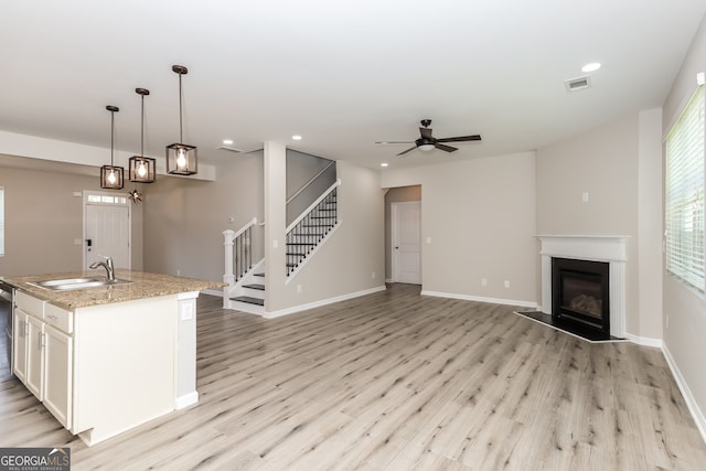 kitchen with light hardwood / wood-style floors, a center island with sink, decorative light fixtures, light stone countertops, and ceiling fan