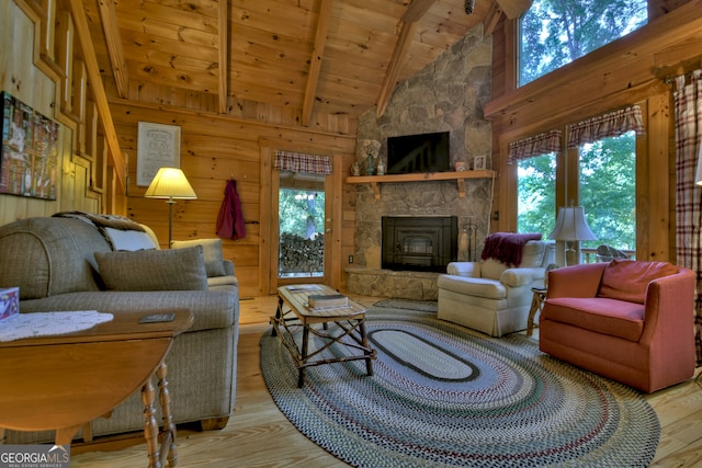 living room with a stone fireplace, beamed ceiling, wood ceiling, and light hardwood / wood-style floors