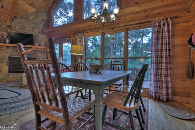 dining room featuring wood ceiling, light hardwood / wood-style floors, high vaulted ceiling, an inviting chandelier, and a stone fireplace