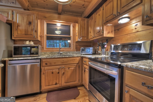 kitchen with light stone countertops, beamed ceiling, appliances with stainless steel finishes, and sink