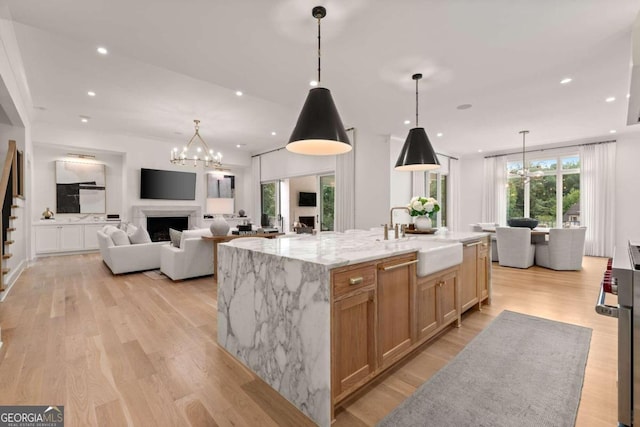 kitchen with pendant lighting, sink, light hardwood / wood-style flooring, light stone countertops, and a spacious island