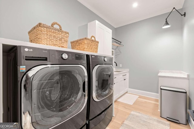 clothes washing area featuring cabinets, light wood-type flooring, and washer and dryer